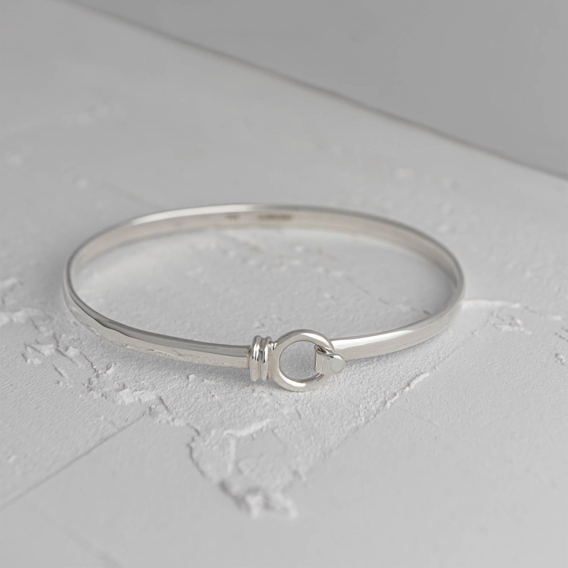 Licks sterling silver bangle by Mon Bijoux sitting on textured white floor