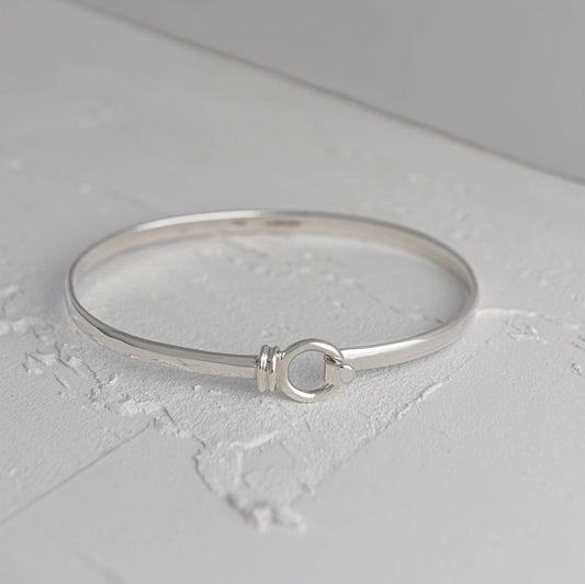 Licks sterling silver bangle by Mon Bijoux sitting on textured white floor