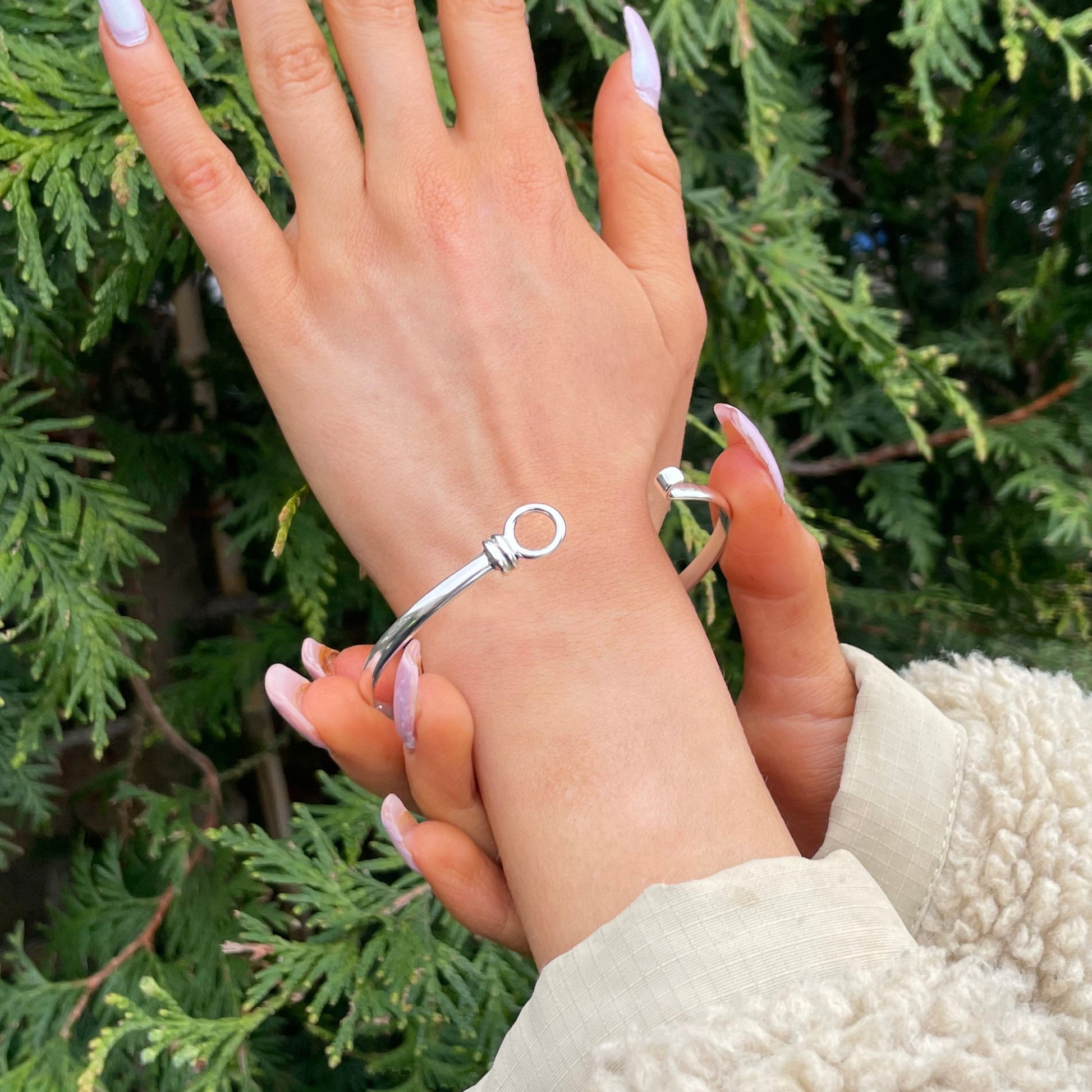 Hand wearing a silver bracelet with green foliage in the background