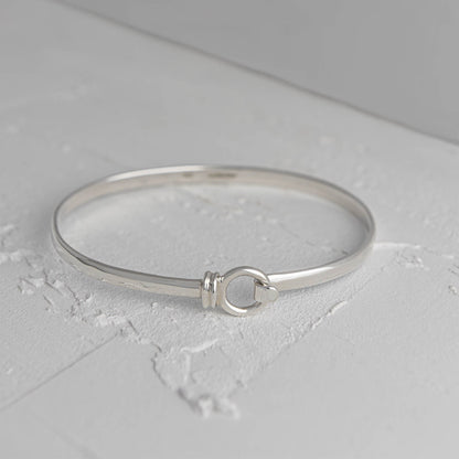 Licks sterling silver bangle by Mon Bijoux sitting on textured white floor